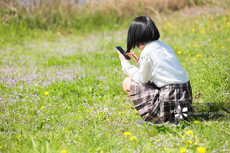 穿着中学校服的10岁女孩，青少年时尚角色扮演的小学生坐在地上用智能手机上网图片素材