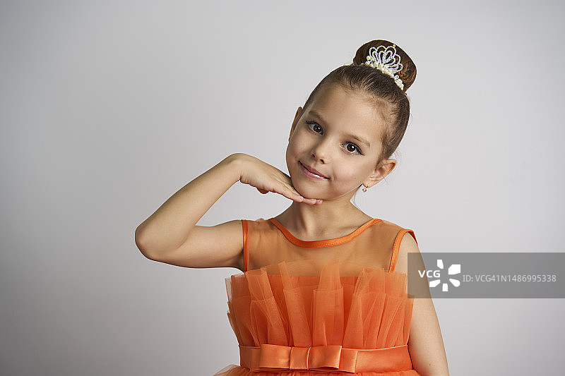穿着橙色连衣裙在白色背景前摆姿势的可爱小女孩图片素材
