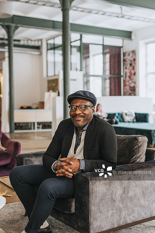 微笑的商人在办公室坐在沙发上，看向别处图片素材