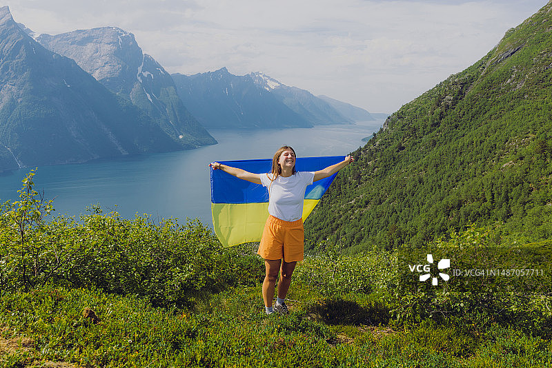 手持乌克兰国旗，在挪威峡湾的上方沉思风景的女人图片素材