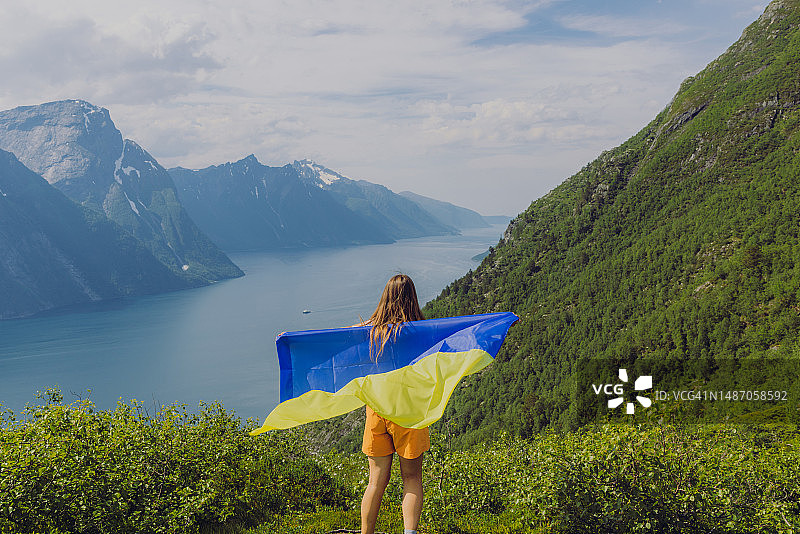 手持乌克兰国旗，在挪威峡湾的上方沉思风景的女人图片素材