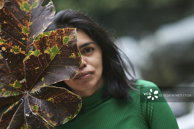 用大树叶遮住部分脸庞的女人肖像图片素材