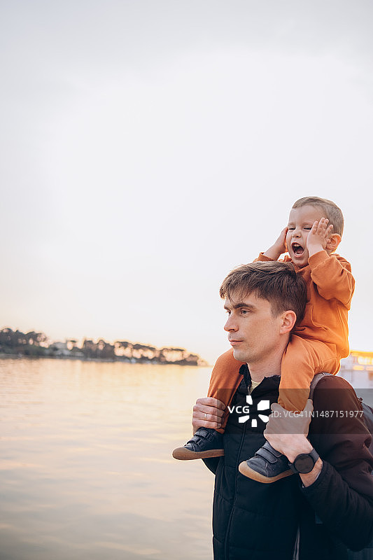 日落时分，儿童坐在父亲的脖子上，在海边玩耍图片素材