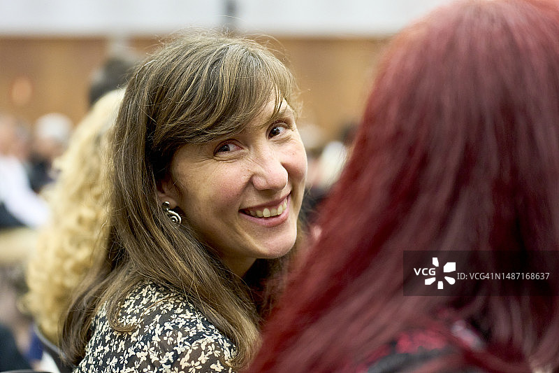 女人坐在礼堂座位上，侧身回头对着镜头微笑特写图片素材