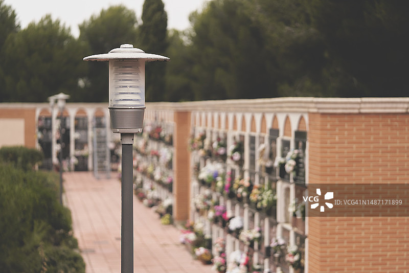 从高角度看到的墓地里熄灭的路灯柱，背景是纪念石墙和引人注目的天空图片素材