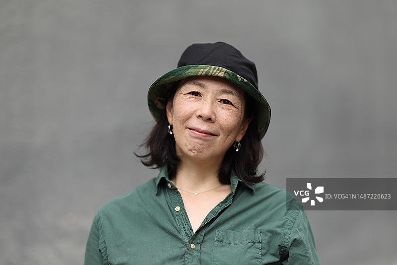 戴帽子的微笑快乐日本女人在灰色墙壁前图片素材