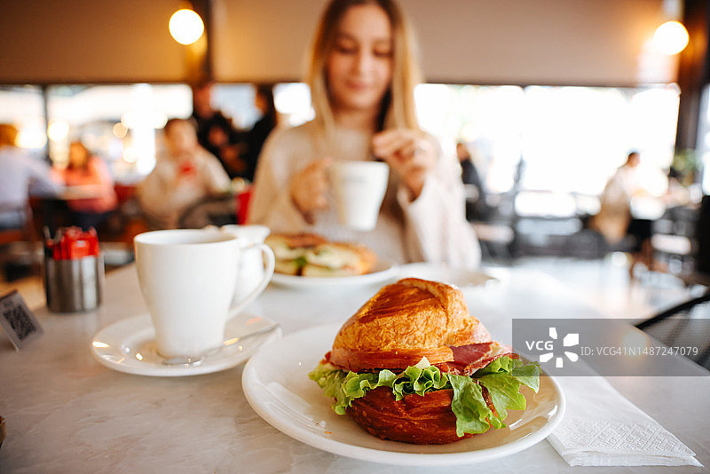 咖啡馆里的卡布奇诺和法式羊角面包，一位女士正在享用早餐图片素材