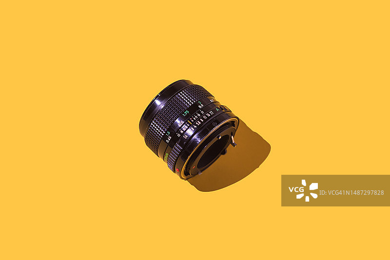 20世纪70年代至80年代的50mm F1.4复古镜头，黄色背景。摄影概念，复古，光圈，快门和摄影师。图片素材