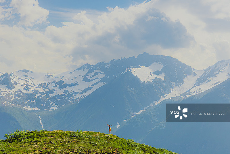 远处快乐的女人在挪威松默尔阿尔卑斯山举臂。图片素材