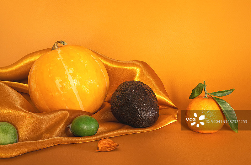 南瓜、鳄梨、斐济果和橘子与绿叶组成的季节性静物抽象构图图片素材