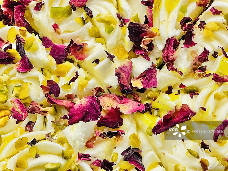 柠檬蛋糕切成薄片，上面覆盖着黄油糖霜和柠檬，并在近距离上撒上切碎的坚果和玫瑰花瓣。图片素材