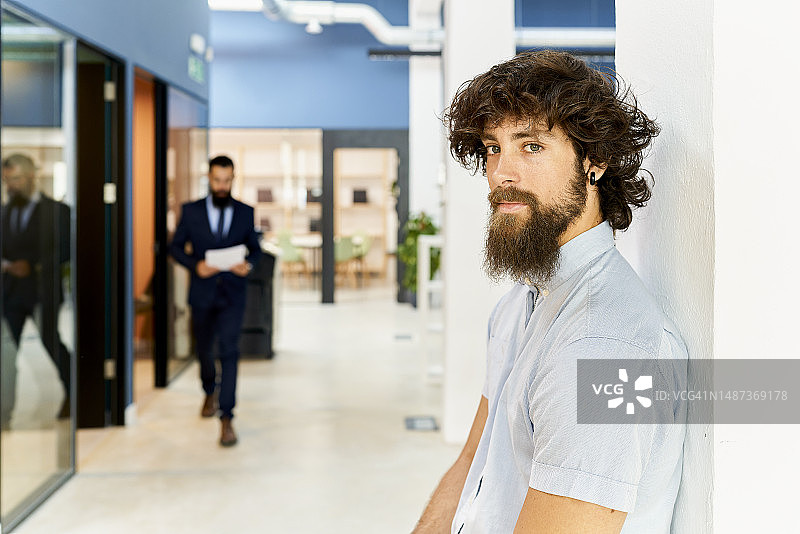 穿着蓝色衬衫的留着胡子的男人，前面是办公室、打印机，后面是戴着眼镜穿着西装的留着胡子的男人图片素材