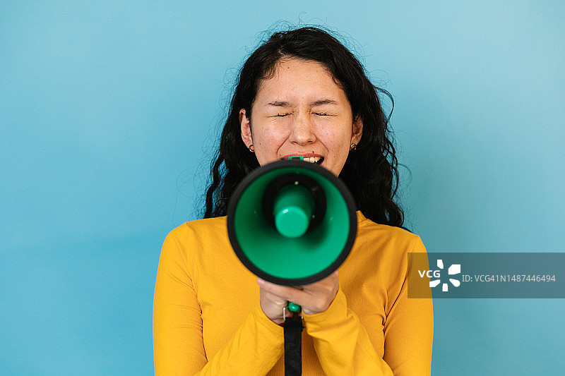 年轻女子在蓝色背景前用扩音器喊话图片素材