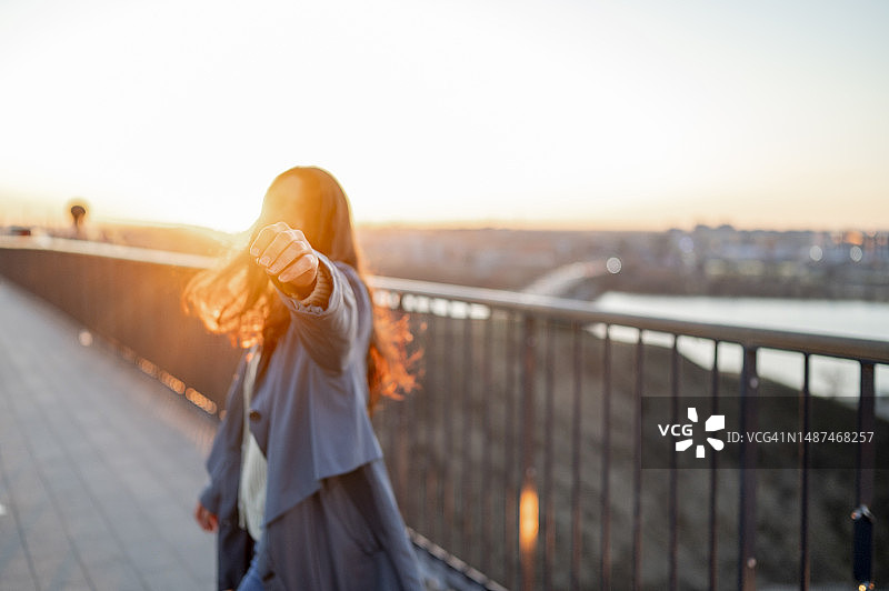 站在桥上，在日落时伸出手的女人图片素材