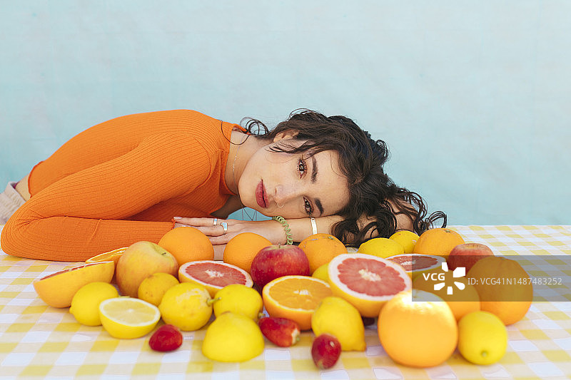 年轻女人倚靠在放有柑橘类水果的桌子上图片素材
