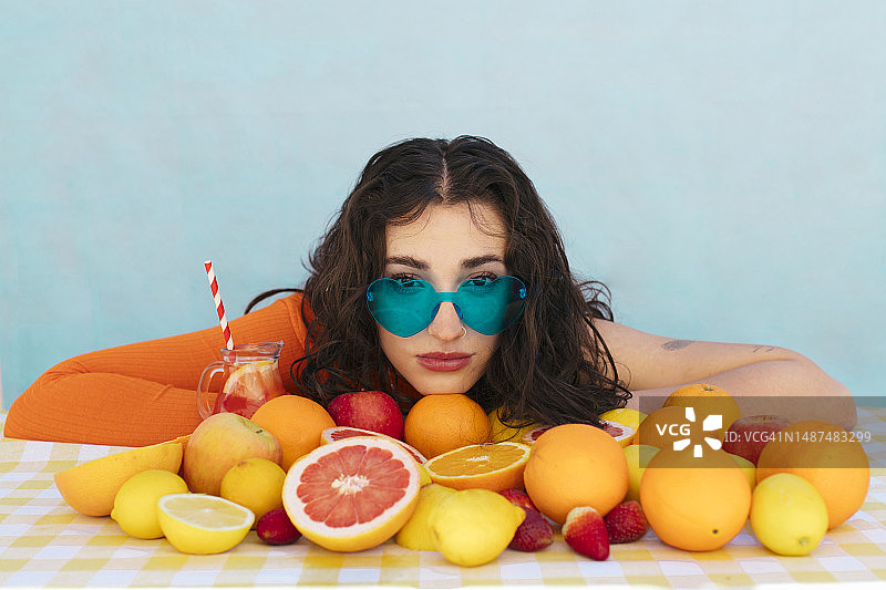 戴墨镜的年轻女人靠在放着柑橘类水果的桌子上图片素材