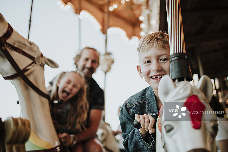 微笑的男孩与家人在游乐园享受旋转木马图片素材