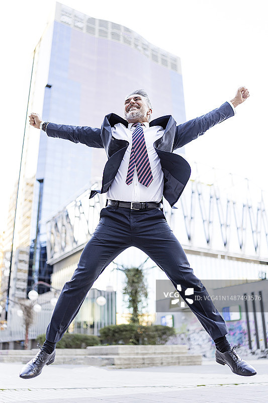 在建筑物前张开双臂跳跃的快乐商人图片素材