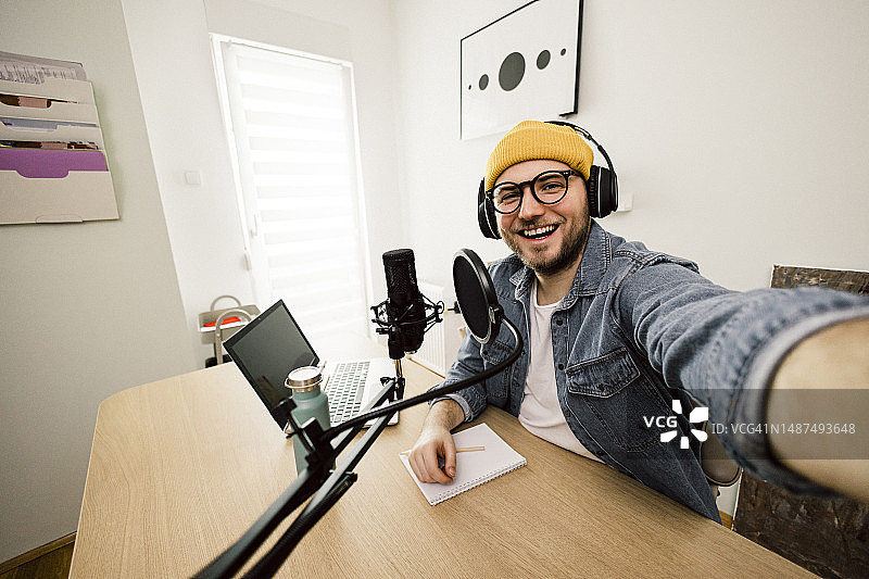 年轻微笑男子在录音棚使用麦克风和耳机录制播客和直播的自画像图片素材