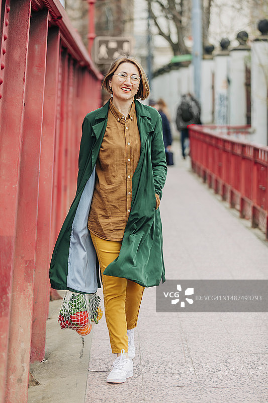 手提网袋蔬菜走在人行道上的微笑女人图片素材