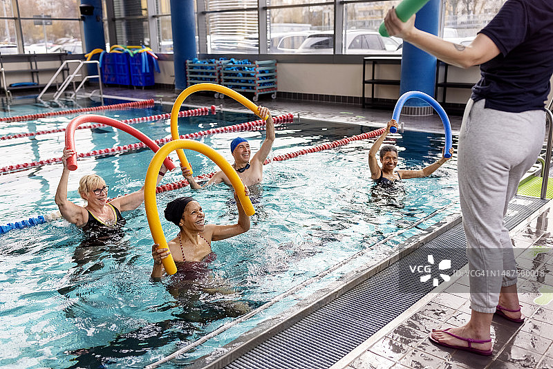 活跃的老年人在教练的指导下在游泳池里用游泳棒锻炼图片素材