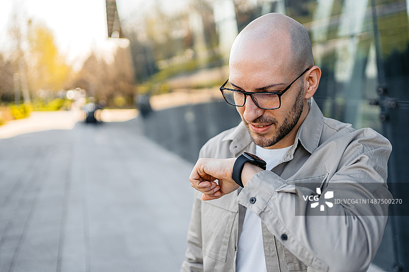 年轻男人在户外公司大楼前使用智能手表图片素材