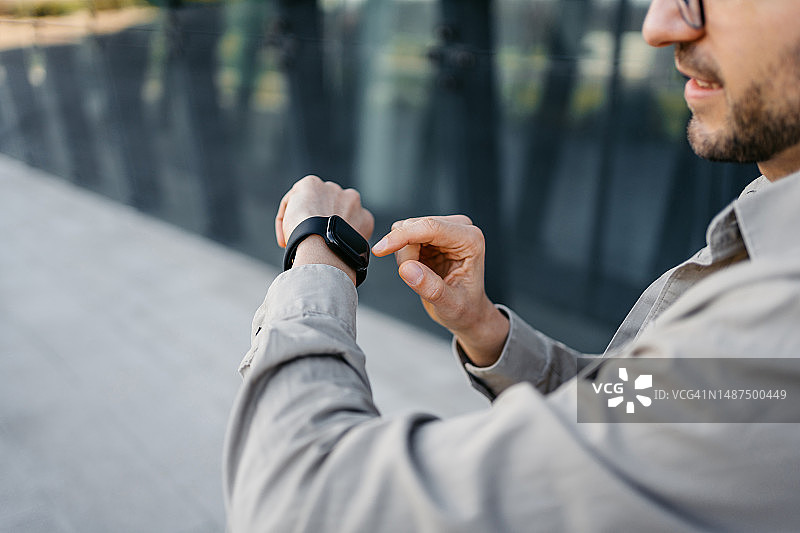 年轻男人在户外公司大楼前使用智能手表图片素材