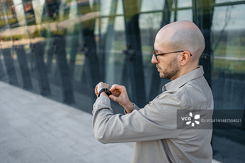 年轻男人在户外公司大楼前使用智能手表图片素材