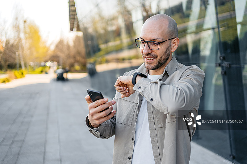在公司大楼外使用手机和智能手表的年轻男人图片素材