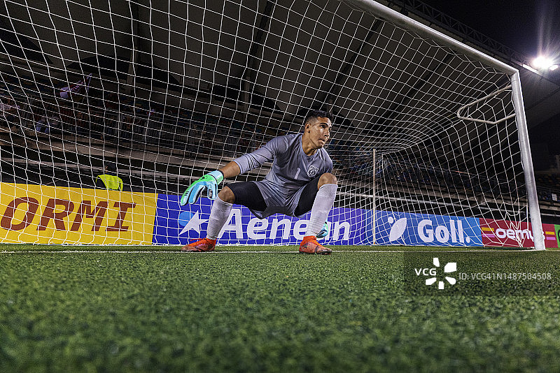 职业男子足球守门员在比赛中蹲下，专注地注视着足球场图片素材