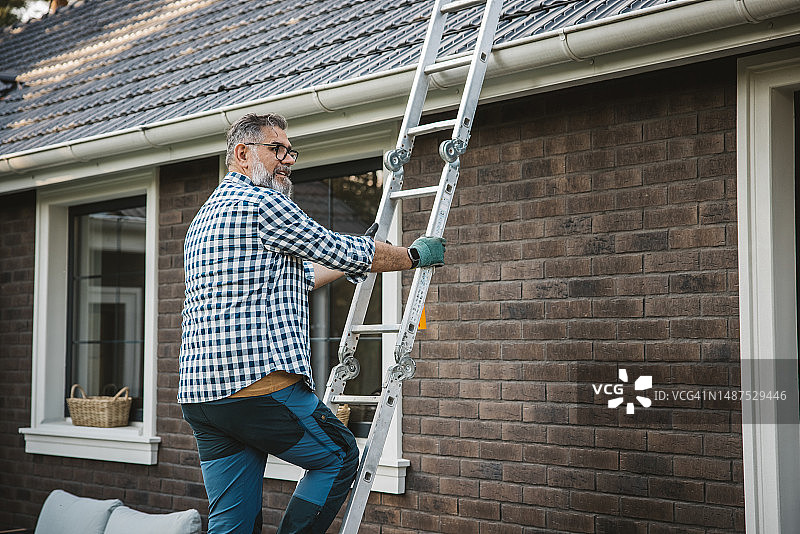 男人清理房屋排水沟中的树叶图片素材