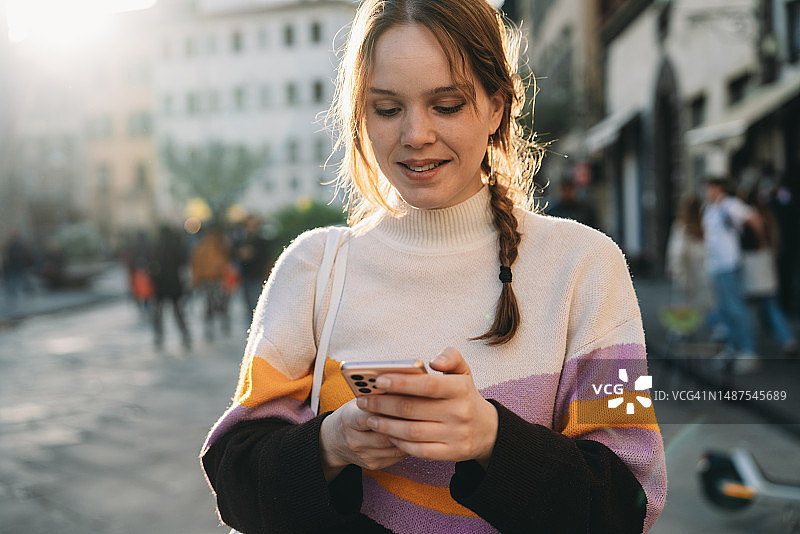 日落时分，女子在城市里用智能手机发短信图片素材
