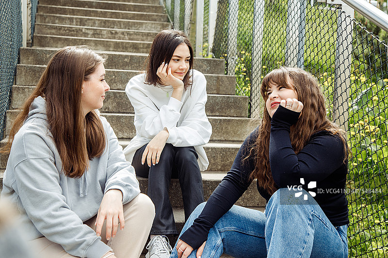 三个年轻女人坐在楼梯上互相看着图片素材
