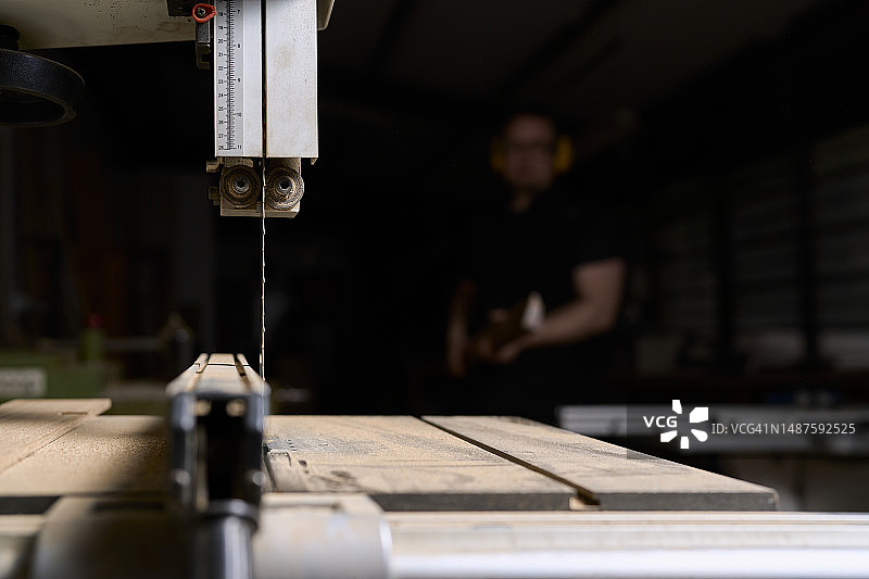 木工车间工作台上锯子的特写，背景中站立着一名男子，正面视角图片素材