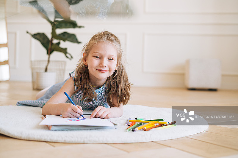 躺在地板上在明亮的房间里画画的学龄前小女孩图片素材