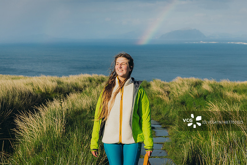 快乐的女人在挪威的伦德岛上在风景如画的海上彩虹下徒步旅行图片素材
