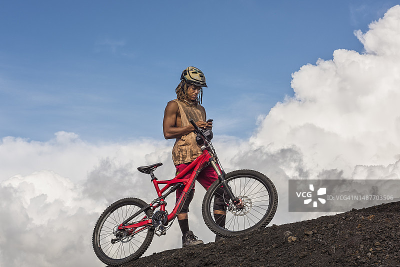 骑山地自行车的男人站在山脊上使用智能手机图片素材