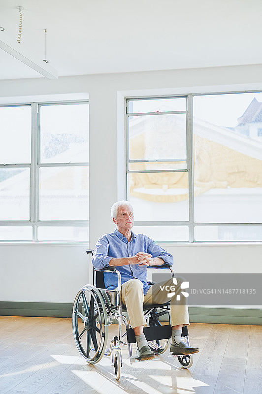 医院里坐在轮椅上双手紧握的年长男人肖像图片素材