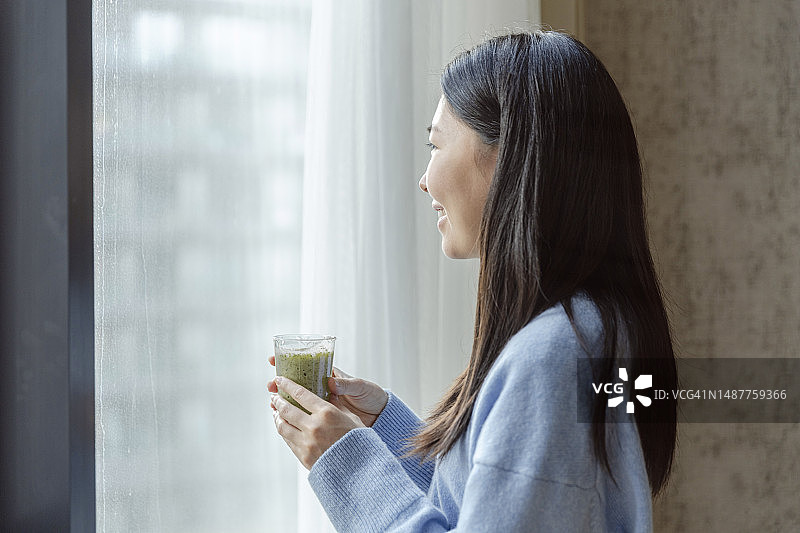 美丽亚洲女人喝绿色排毒果汁看向窗外图片素材