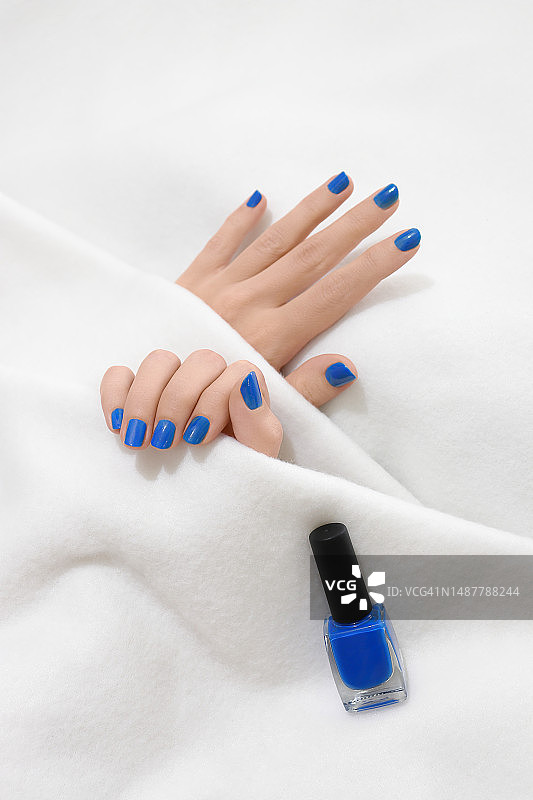 白色毯子上，涂有蓝色指甲油的女人手图片素材