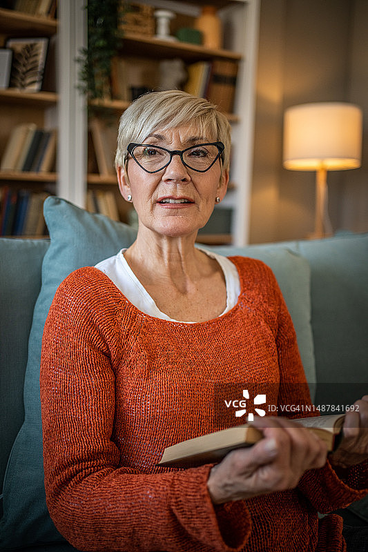 一位年老的退休人员舒适地坐在沙发上，专心致志地读着她最喜欢的书图片素材