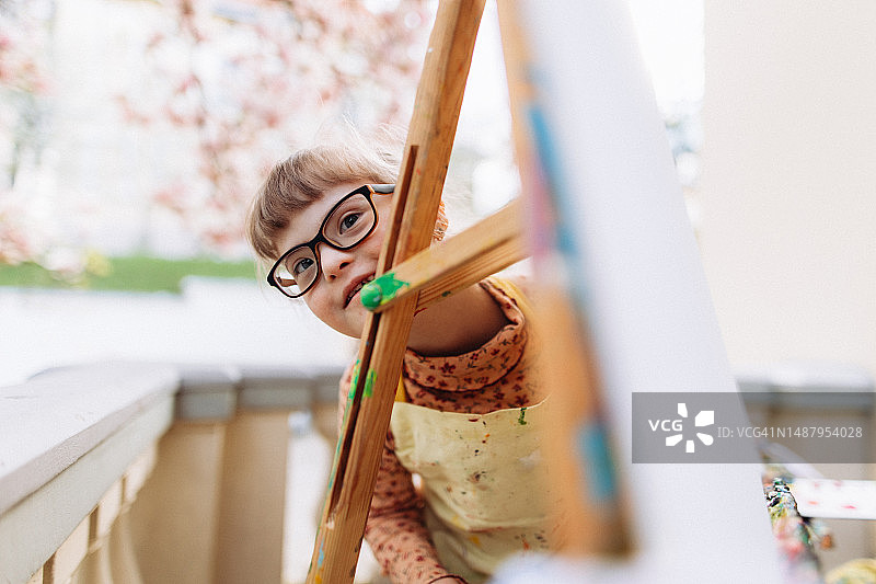 在艺术治疗中藏在画架旁的唐氏综合征微笑女孩图片素材