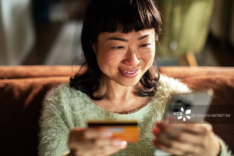 用信用卡在智能手机上购物的年轻日本女人图片素材
