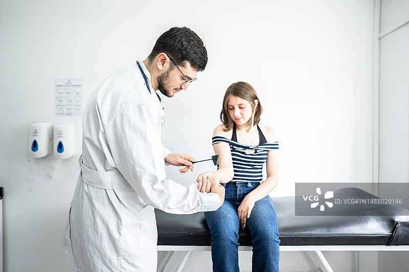 医生/理疗师在医疗诊所使用反射锤检查病人的手臂图片素材