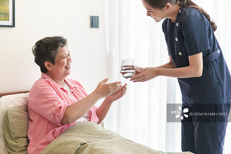 年轻的亚洲女护士给卧室里的老年病人递一杯水图片素材