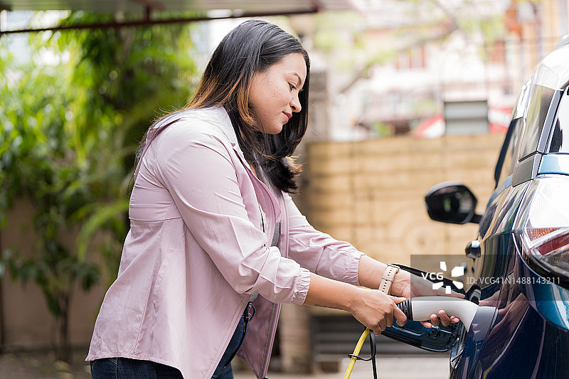年轻女人为电动汽车充电图片素材