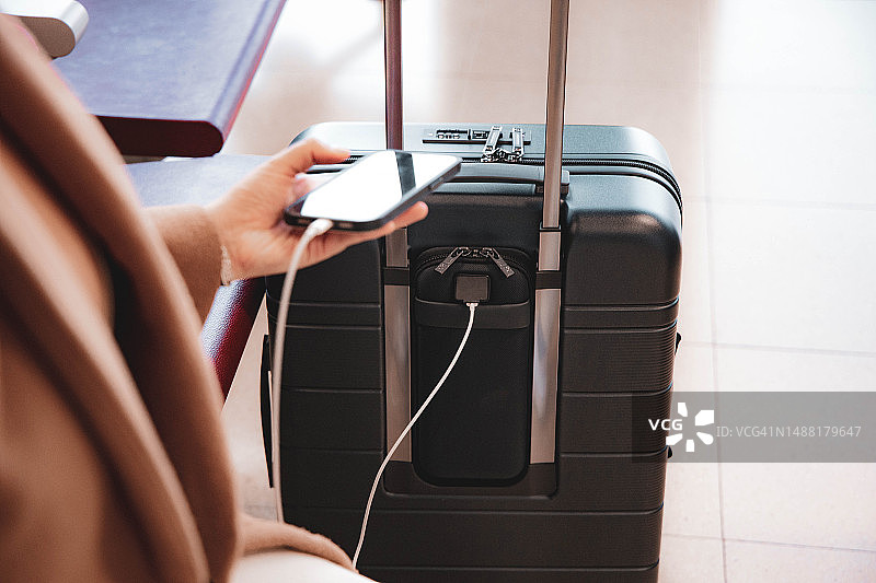 在机场出发航站楼用智能行李箱为智能手机充电的女人图片素材
