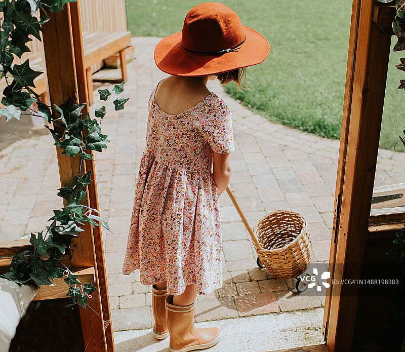 小女孩戴着大帽子，穿着印花连衣裙站在露台上拉着柳条篮子图片素材