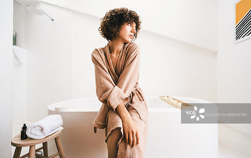 一位年轻的卷发白人女子坐在豪华浴室里图片素材
