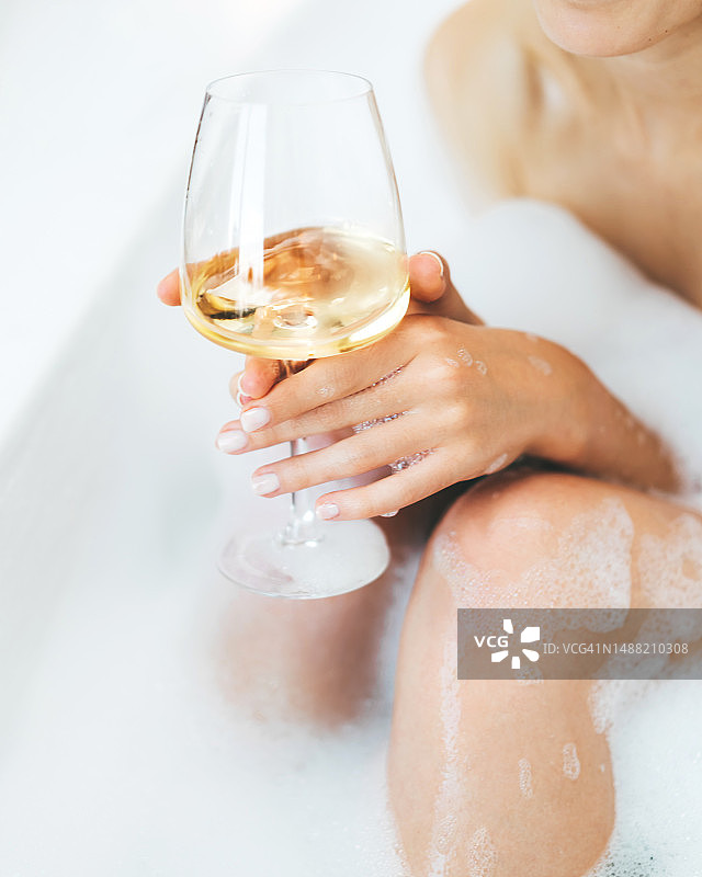 一位不知名的妇女在热水浴缸里喝白葡萄酒，手里拿着一个玻璃杯图片素材